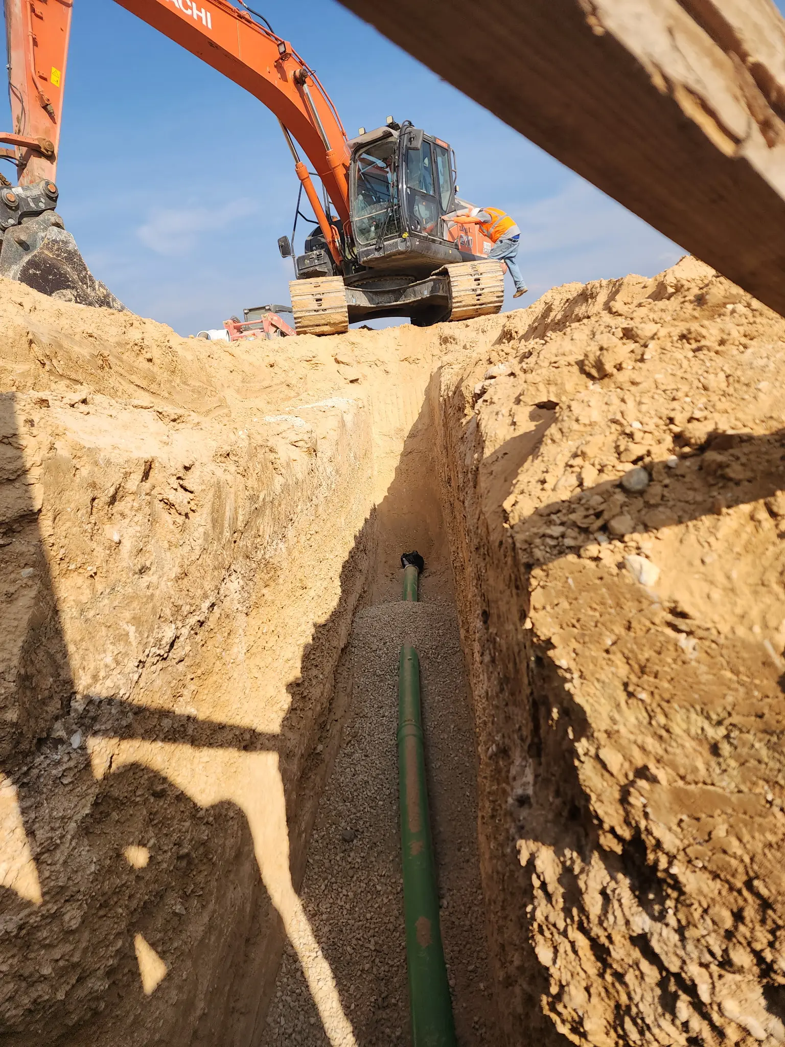 Excavator digging a trench with a pipe installation.