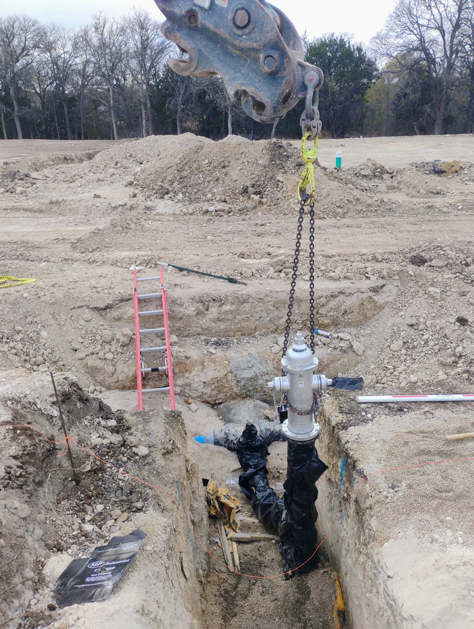 Workers operate a crane to lift a large pipe at a construction site.